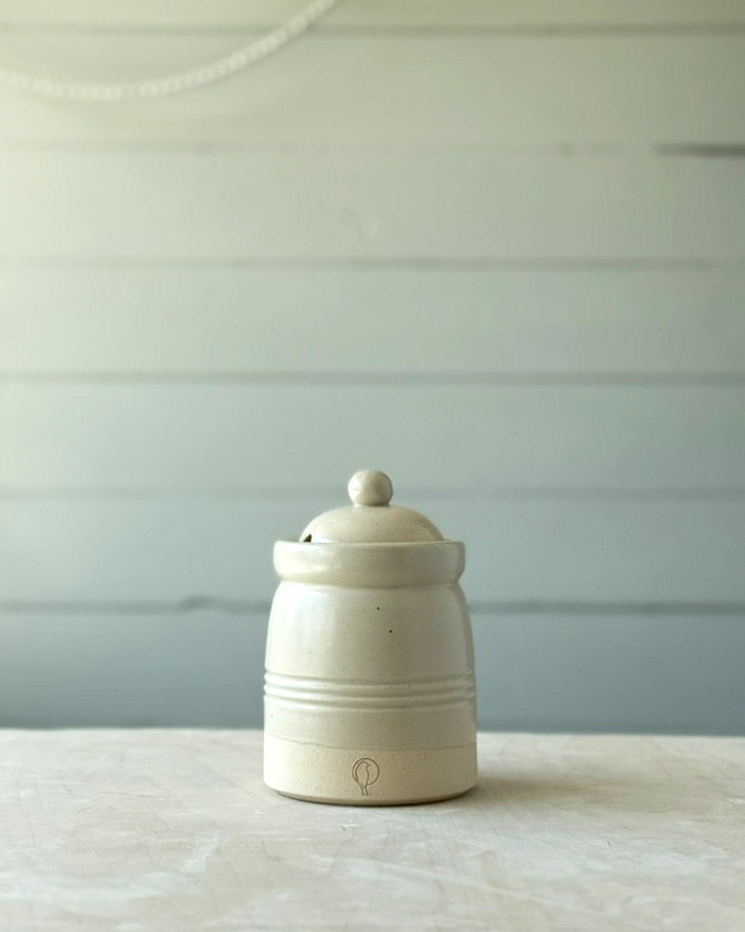 White ceramic jar with a lid on a light wooden surface with a light blue background