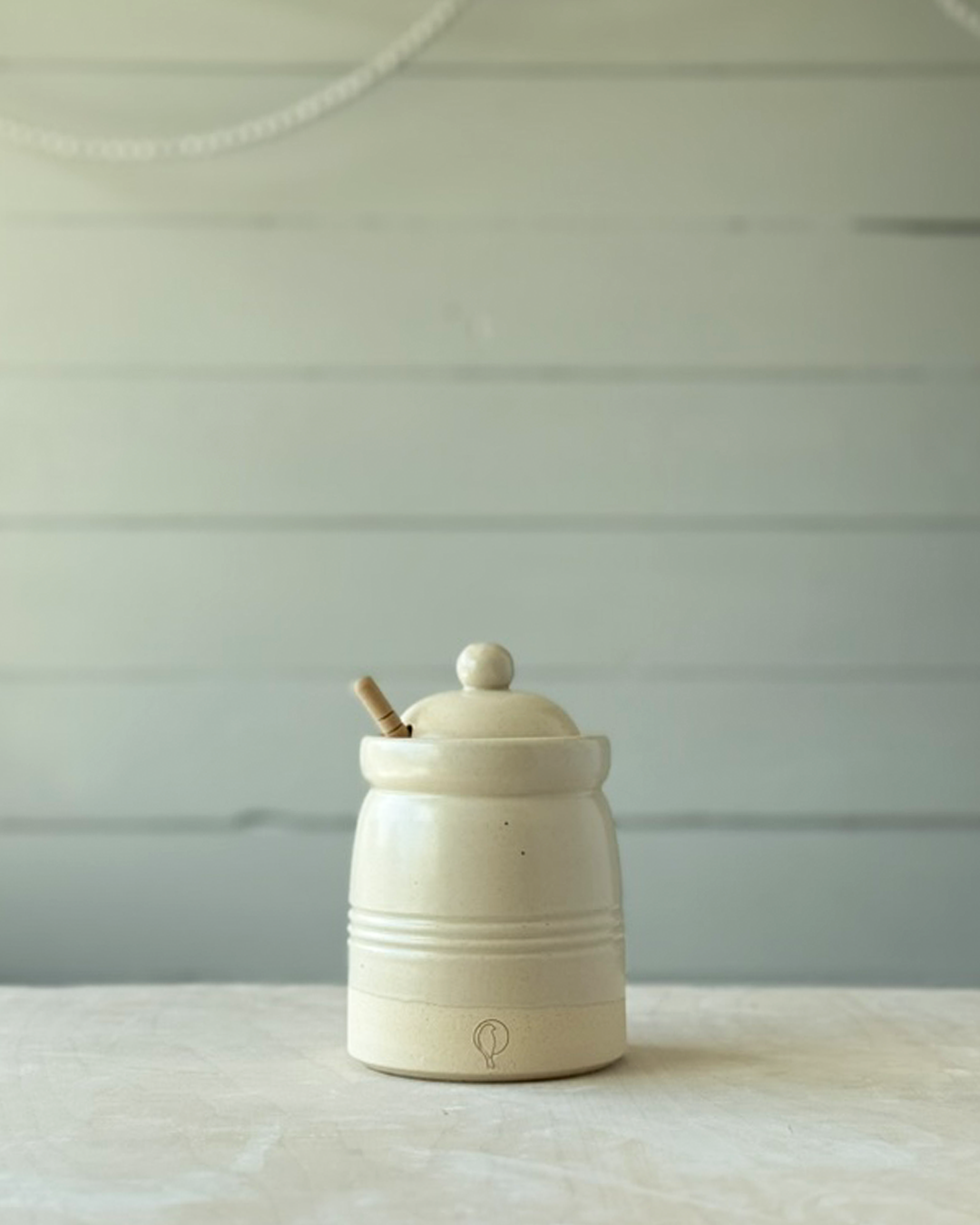 White ceramic jar with a lid and wooden spoon on a light surface with a light gray background