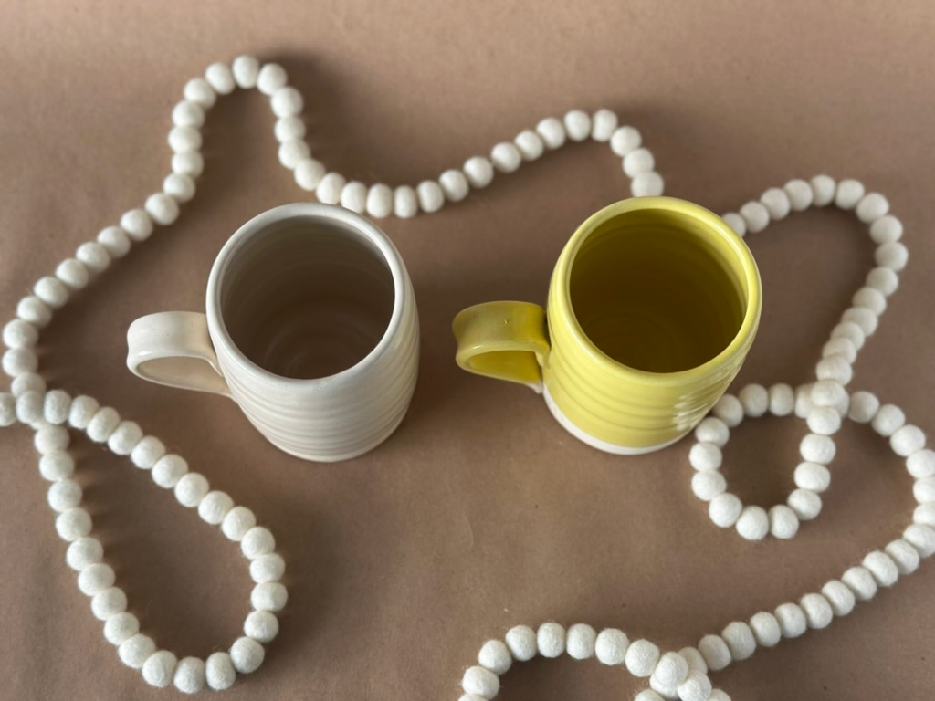 Two mugs top view white and Yellow with a white needle felted wool garland and a brown backdrop