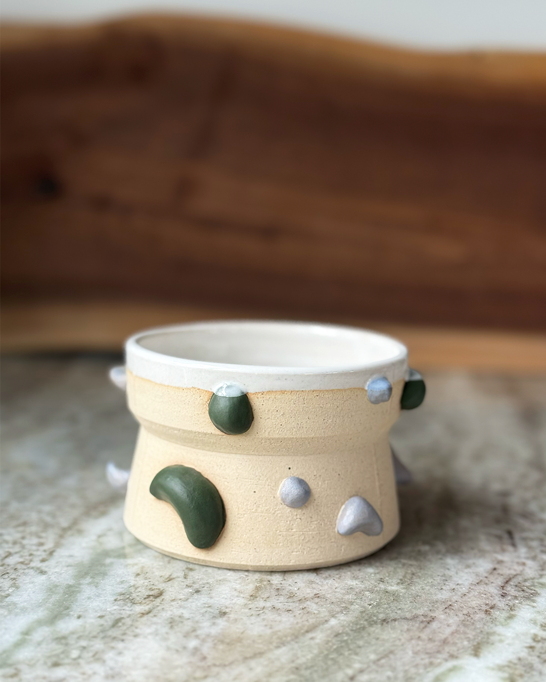 Climbing Wall inspired mug with handholds in green and white on a tan clay body with white glaze and a marble and wood backdrop