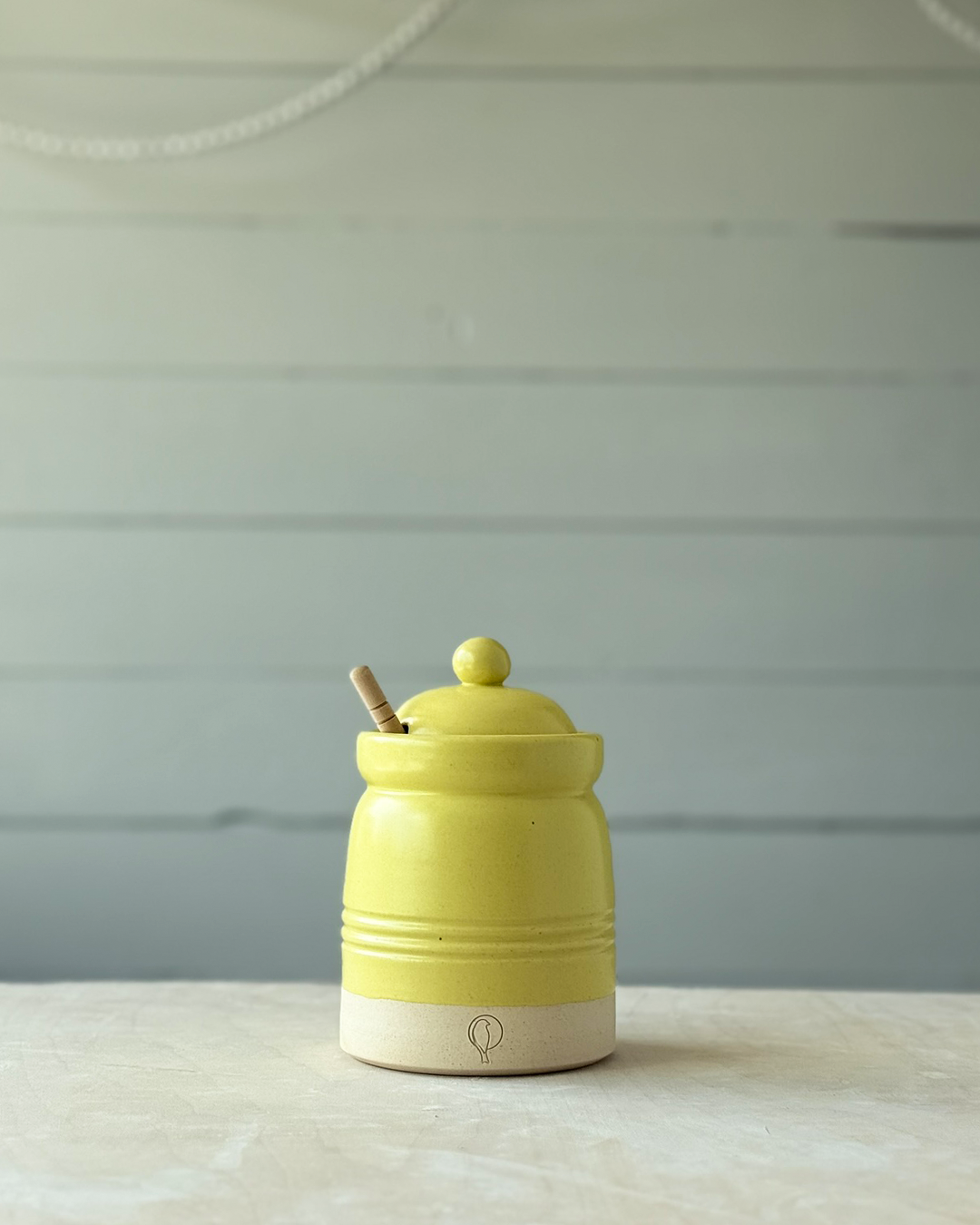 Yellow ceramic jar with a lid and wooden spoon on a white surface with a light gray background