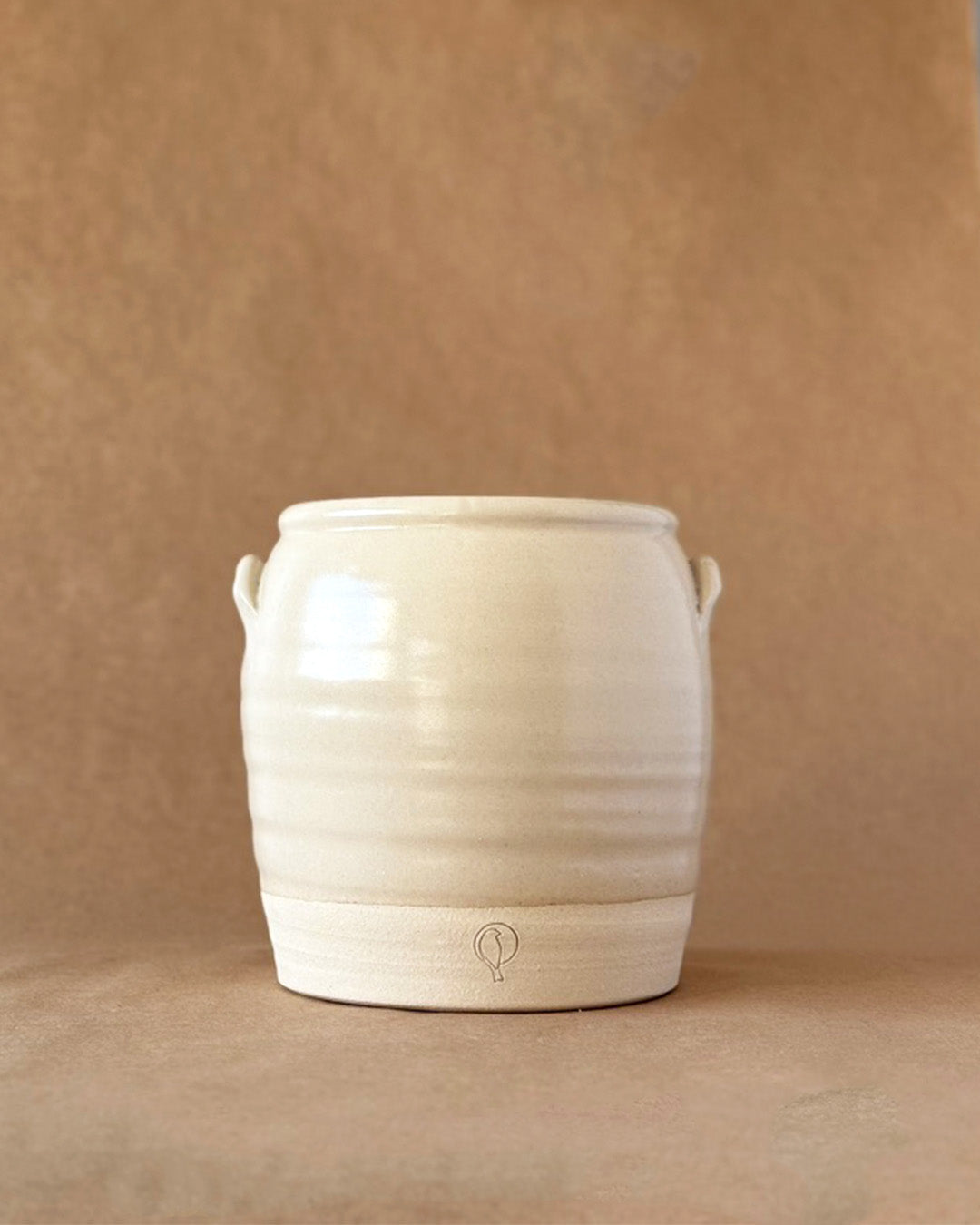 Old World Inspired Crock in a linen Glaze with a bird logo stamped at the bottom with a brown backdrop 