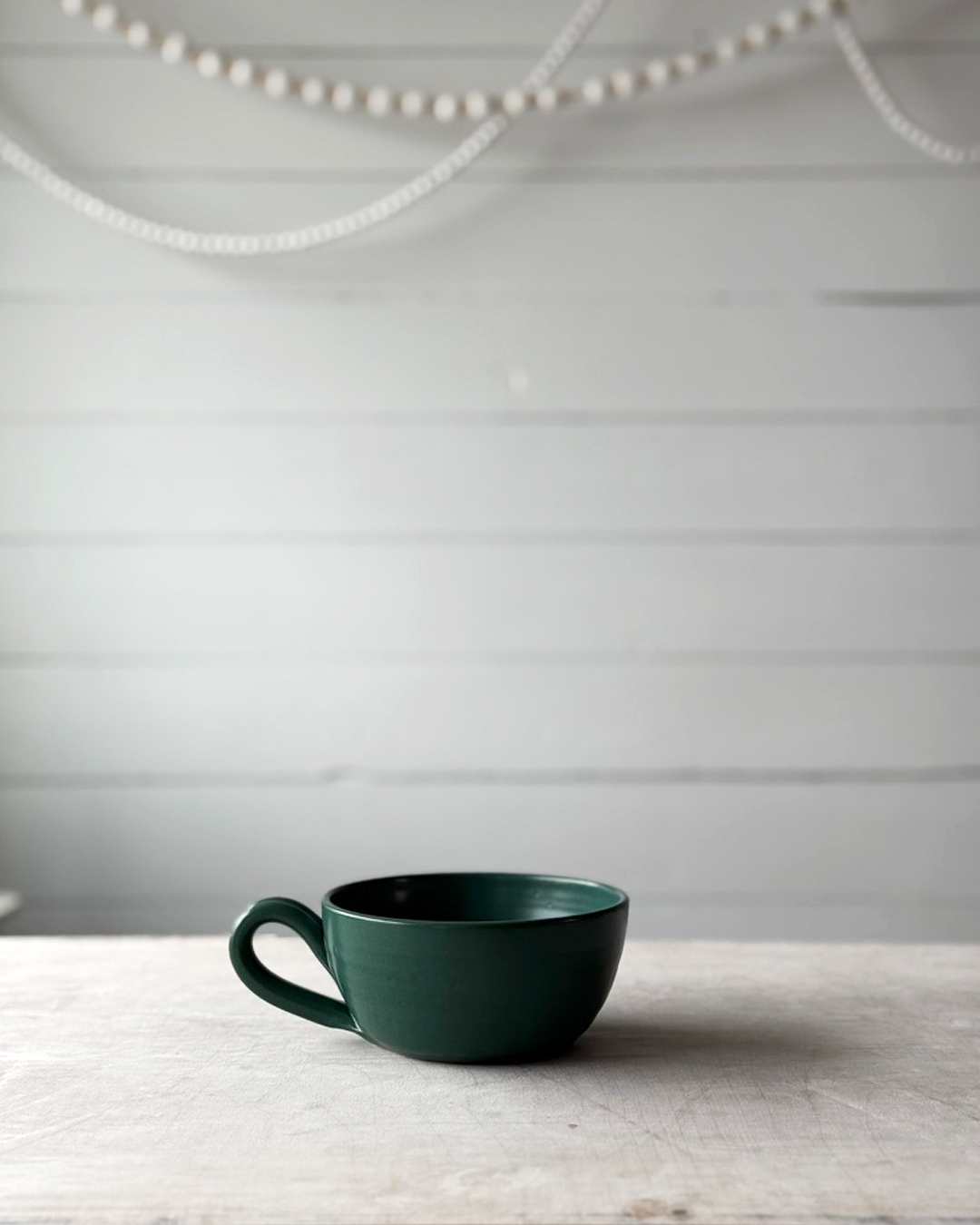 Green ceramic cup on a wooden surface with a light gray background