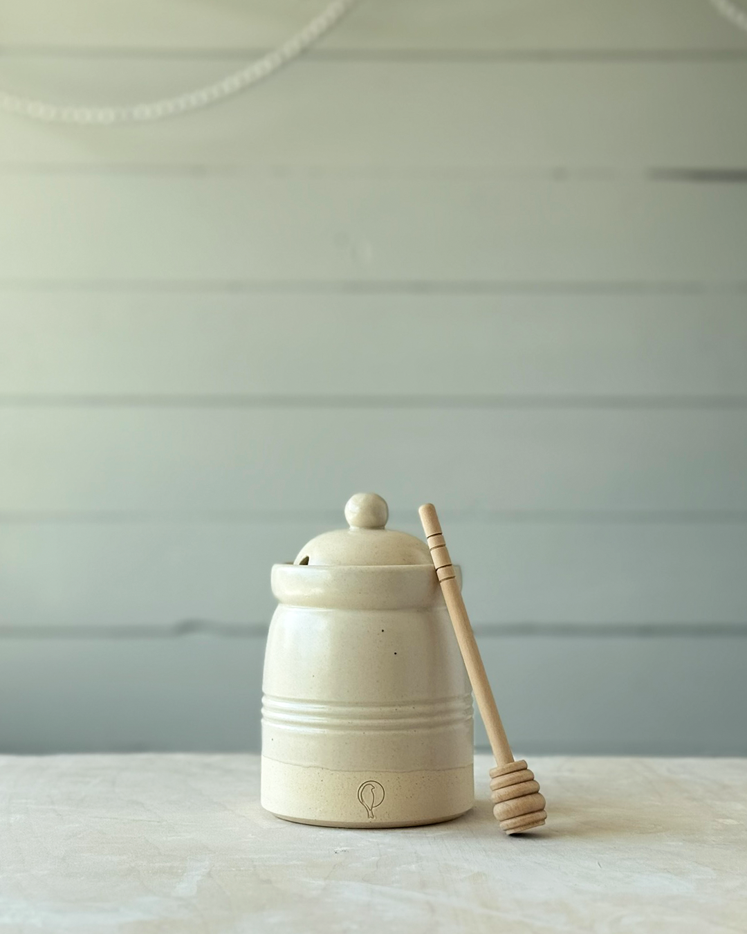 White ceramic honey jar with a wooden honey dipper on a light surface and light gray background