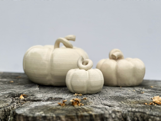 three linen ceramic pumpkins resting on a tree stump 