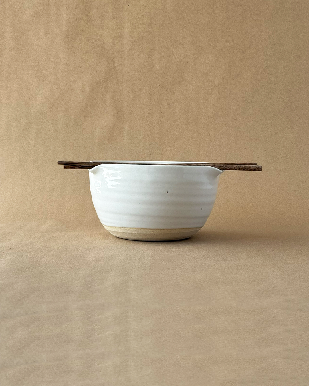 White ceramic colander with wooden handle on a beige background