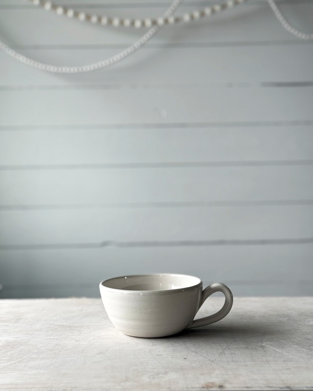 White ceramic cup on a wooden surface with a light gray background
