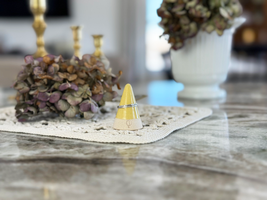 Yellow Ring Cone with Silver stacked Rings on a white doily with dried flowers on a quartz countertop