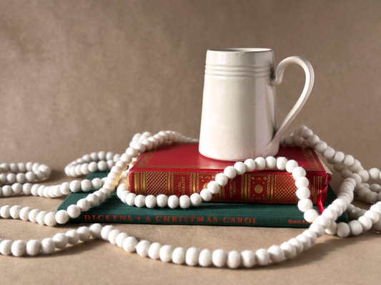 Linen Tankard mug on a red book with Gold embossed side, another book Dickens A Christmas Carol in green with a needle felted white garland. Brown Backdrop 