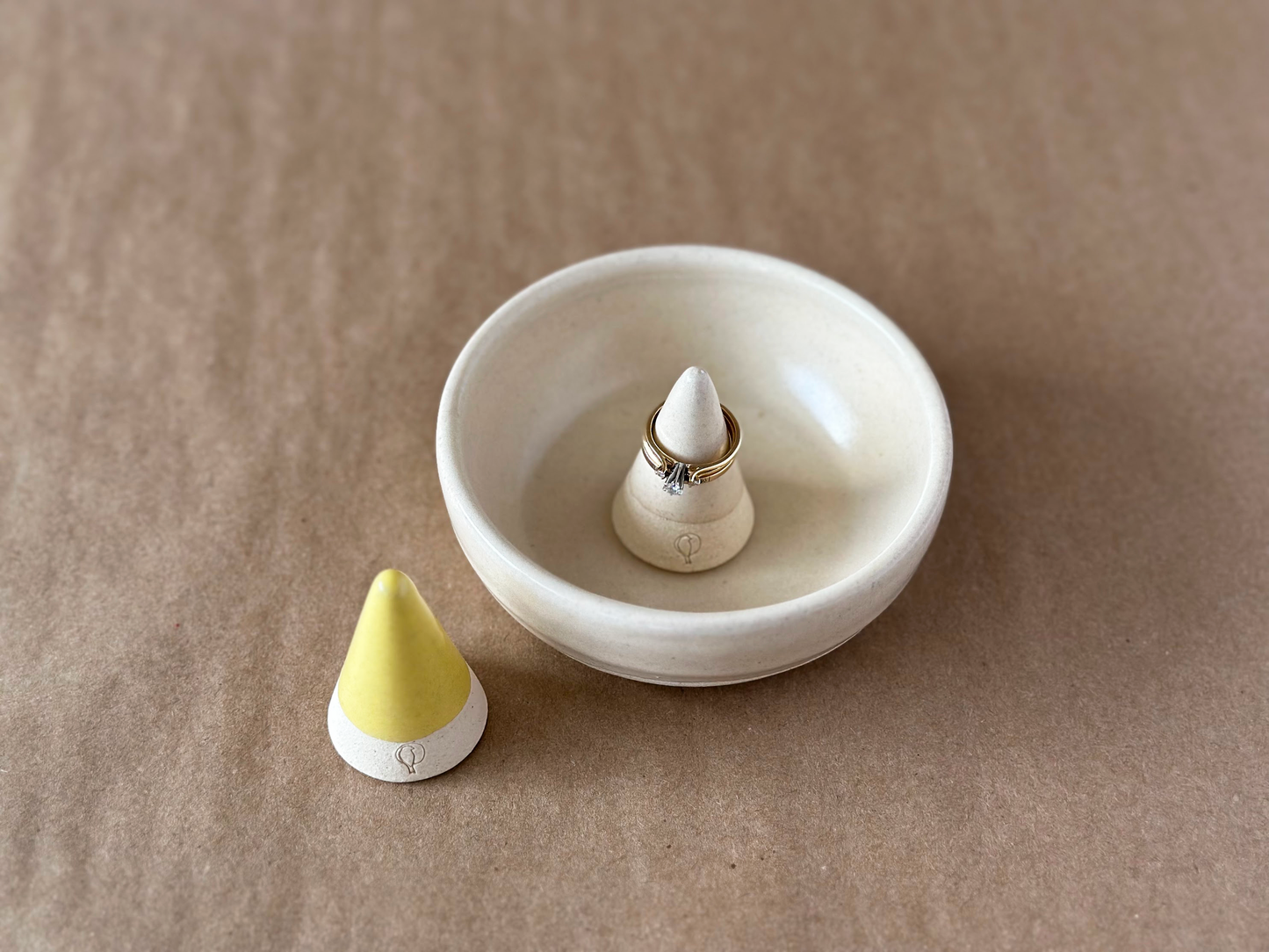 Yellow ring cone and Linen ring cone in small bowl displaying gold wedding ring set on a brown backdrop